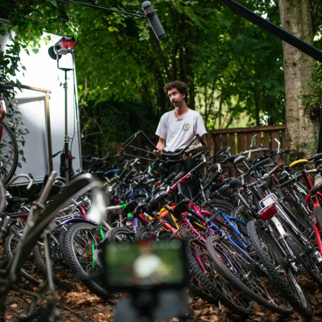 Cinematic behind-the-scenes shot from Holy Moly Films' 'Fanzy Bikes' short film, showing actor Jakob Deutschmann as a bike mechanic among countless bicycles.
