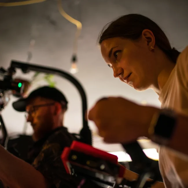 Close-up behind-the-scenes shot of the Holy Moly Films crew, showcasing directress Mascha Deikova working in tandem with cinematographer Imanuel Thallinger with a professional camera rig.