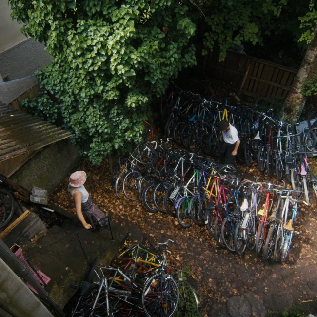 A creative high-angle wide shot showcasing a backyard packed with dozens of vibrant upcycled bicycles during a Holy Moly Films production.