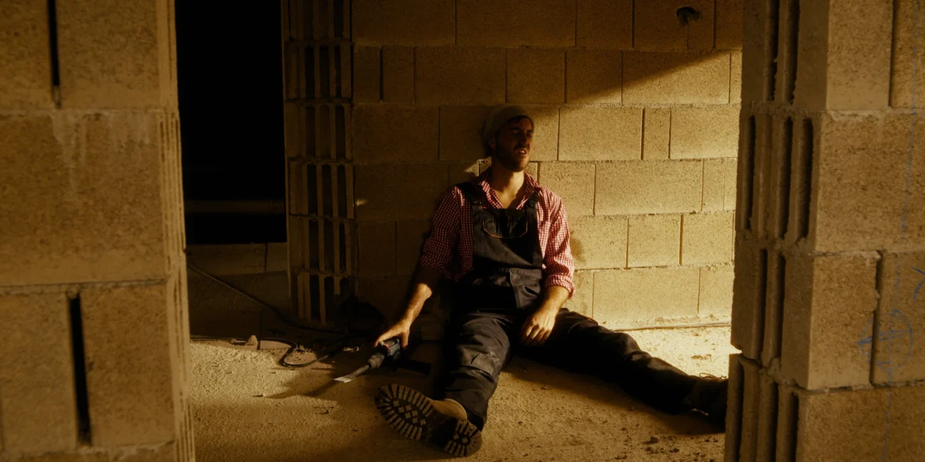 Austrian Kiwi construction worker sitting exhausted against a concrete wall on set during the comedy skit filming produced by Holy Moly Films.
