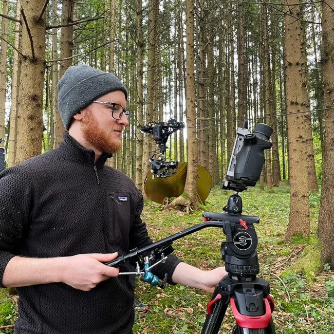 Cinematographer Imanuel Thallinger operating the camera on a cable cam system running through the trees in the background.