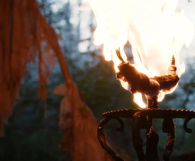 A burning wrought-iron ritual torch flickering in a dark misty forest set for the short film HECATE.