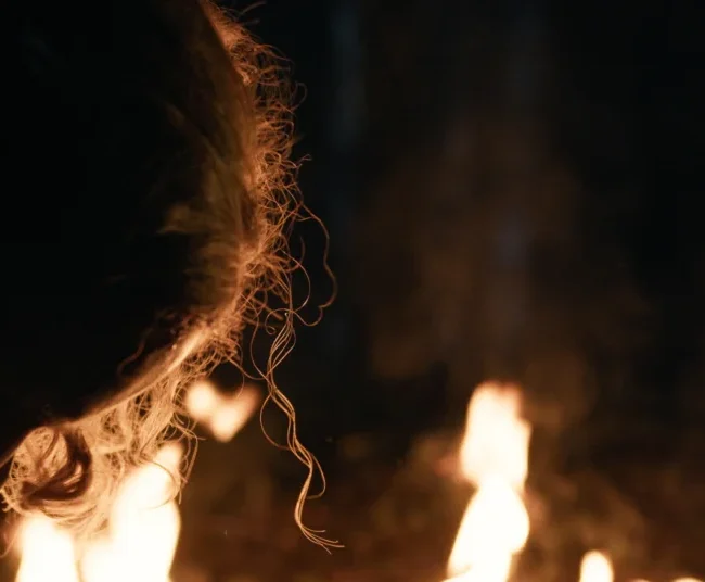 Intimate cinematic close-up shot of actress Julia Rajsp lit by warm flickering firelight during a night scene in HECATE.