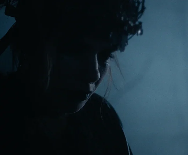 Atmospheric low-key side profile of Selina Pöstinger as the witch illuminated by cool moonlight on set.