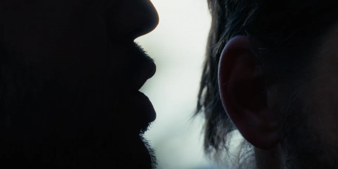 Dramatic silhouette close-up of a man whispering a secret directly into another person's ear.
